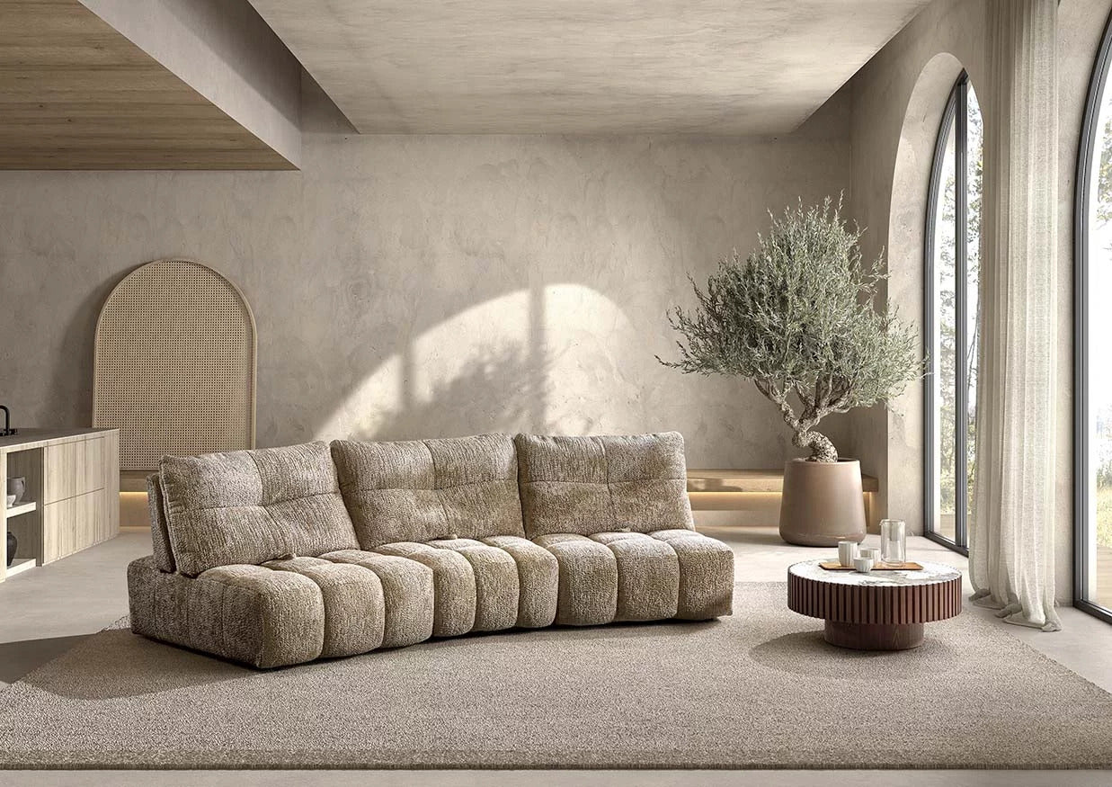 Beau canapé Heidi beige sable, avec des formes rondes, 3 dossiers qui se reculent, sans accoudoir. Il parait très confortable et douillet, jolie table basse ronde 